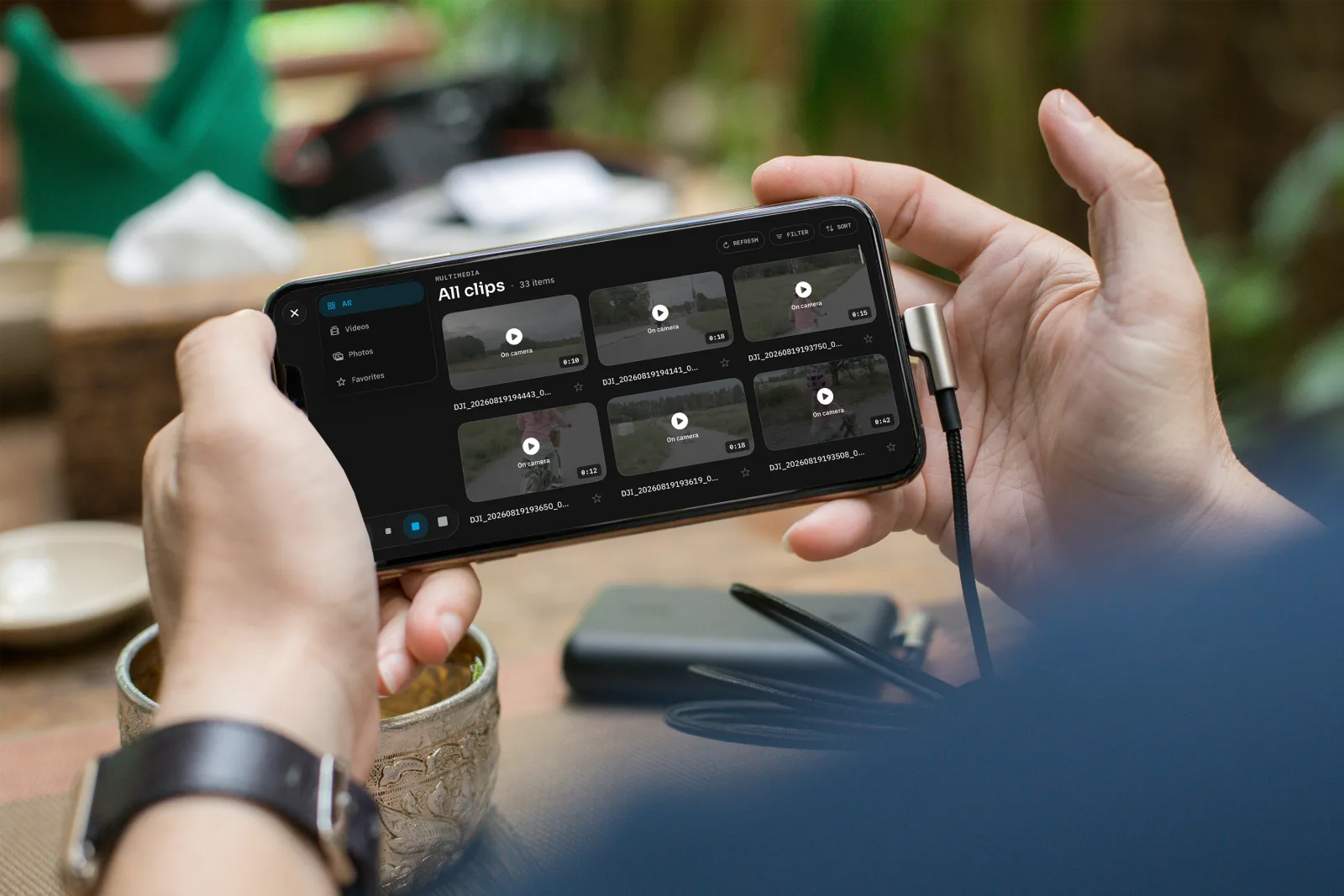 OpenPocketCine media library on iPhone: all clips, videos, photos, and favorites over a cafe table
